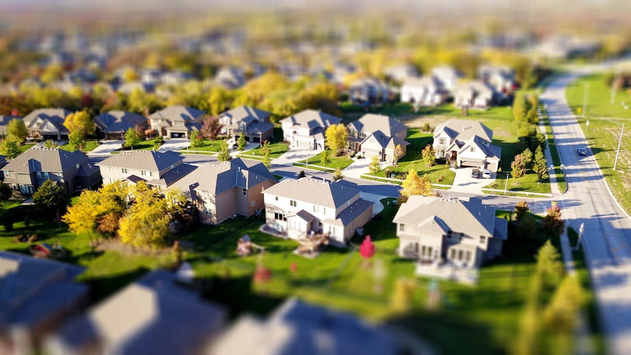 hero-img-02 Tilt-shift aerial photo of a suburban neighborhood with green lawns and roads.